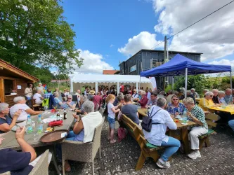 Eine lebhafte Versammlung von Menschen unter einem Zelt im Freien. Die Atmosphäre ist entspannt und gesellig mit Tischen voller Getränke und Snacks.