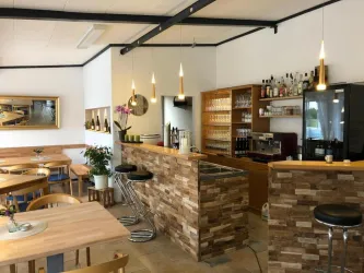 Ein modernes Café mit hellen Holzmöbeln und ansprechender Theke. Die Umgebung ist einladend und gut beleuchtet, mit Pflanzen und dekorativen Elementen.
