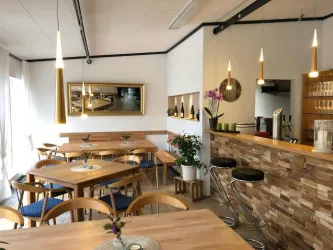 Ein modernes Café mit Holztischen und stilvollen Sitzgelegenheiten. Die Einrichtung ist hell und einladend, mit einigen Pflanzen und dekorativen Elementen.