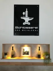 Ein modernes Weingeschäft mit einem eleganten Schild an der Wand. Darunter befindet sich eine Holzregal mit zwei Weinflaschen und einer Bilderrahmen.