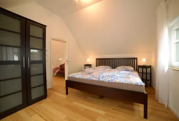 Ein modernes Schlafzimmer mit einem Doppelbett und einem großen Kleiderschrank. Die Wände sind hell und der Boden ist aus Holz, was einen gemütlichen Eindruck vermittelt.