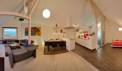 Ein modernes Wohnzimmer mit offener Küche und Essbereich. Große Fenster lassen viel Licht herein und es gibt farbenfrohe Kunstwerke an den Wänden.