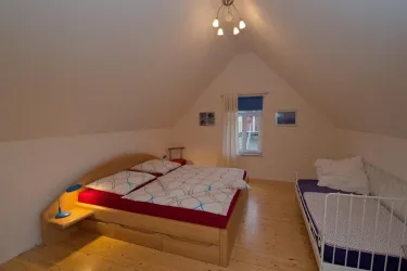 Ein gemütliches Schlafzimmer mit einem Doppelbett und einem Einzelbett. Der Raum hat eine helle Atmosphäre und Holzfußboden.