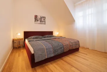 Ein modernes Schlafzimmer mit einem gemütlichen Doppelbett und Holzfußboden. Große Fenster sorgen für viel Licht und eine freundliche Atmosphäre.
