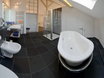 Ein modernes Badezimmer mit einer freistehenden Badewanne und einer Glasdusche. Die Wände sind hell und der Boden ist mit dunklen Fliesen ausgelegt.