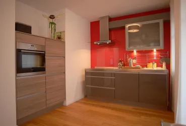 Moderne Küche mit Holzfußboden und roter Wand. Sie enthält elegante Möbel und zahlreiche Küchenutensilien.