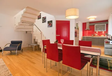 Ein modernes Wohnzimmer mit einer offenen Küche und einem Esstisch. Die Wände sind rot und die Möbel sind stilvoll und einladend.