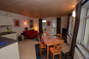 Eine gemütliche, moderne Wohnung mit einem roten Sofa und einem Esstisch. Große Fenster lassen viel Licht hereinfällt.