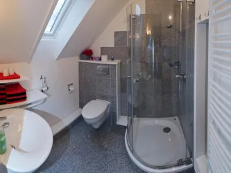 Ein modernes Badezimmer mit einer Duschkabine und einem Waschbecken. Es gibt graue Wände und ein großes Fenster, das für natürliches Licht sorgt.