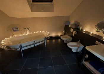 Ein modernes Badezimmer mit einer freistehenden Badewanne und stimmungsvollem Kerzenlicht. Die dunklen Fliesen und minimalistischen Möbel verleihen dem Raum ein elegantes Ambiente.