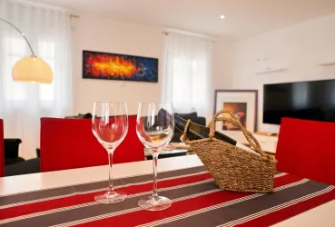 Ein modernes Wohnzimmer mit rotem Möbel und einer stilvollen Dekoration. Auf dem Tisch stehen zwei Weingläser und ein Korb, was eine einladende Atmosphäre schafft.