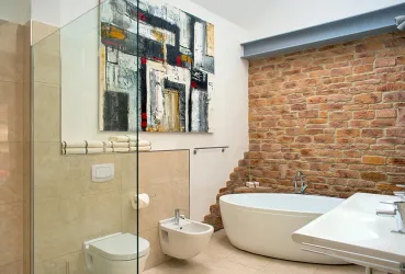 Ein modernes Badezimmer mit einem eleganten Freistehenden Badewanne und einer bodengleichen Dusche. Die Wände sind teilweise mit Steinen verkleidet und es hängt ein stilvolles Kunstwerk.