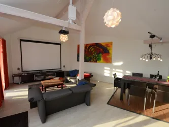 Ein modernes Wohnzimmer mit einer gemütlichen Sitzecke und einem großen Fernseher an der Wand. Der Essbereich ist elegant mit einem Tisch und Stühlen gestaltet.