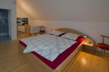 Ein gemütliches Schlafzimmer mit einem großen Bett und einer warmen Decke. Der moderne Holzfußboden und das dezente Licht schaffen eine angenehme Atmosphäre.