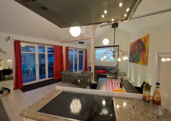 Eine moderne Wohnung mit einer offenen Küche und einem gemütlichen Wohnbereich. Große Fenster sorgen für viel Licht und Ausblick auf den Balkon.