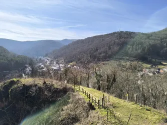 Eine malerische Landschaft mit sanften Hügeln und einem kleinen Dorf im Tal. Die Bäume sind spärlich und der Himmel ist klar und blau.