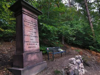Der historische Gedenkstein - Loblochstein - steht inmitten des bewaldeten Gebiets von Lindenberg (Pfalz). Daneben befindet sich eine Bank, die zu einer Pause im Grünen einlädt.
