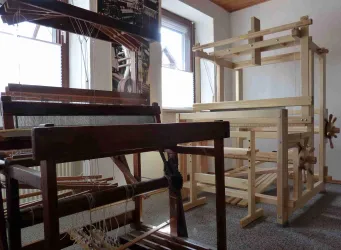 Eine alte Webstube mit mehreren Webstühlen aus Holz. Die Fenster lassen viel Tageslicht herein und schaffen eine helle Atmosphäre. Diese alten Webstühle stehen im Webermuseum in Lindenberg (Pfalz)