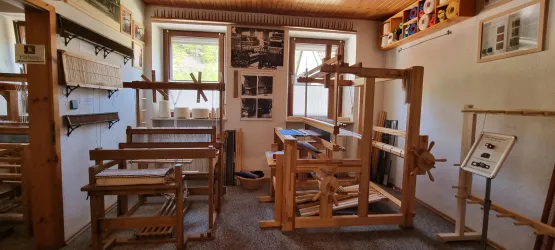 Ein traditioneller Raum mit Holzwebstühlen und Werkzeugen. Die Wände sind mit Bildern und Informationen über das Handwerk dekoriert.