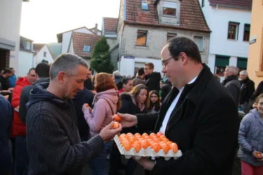 Eine Menschenmenge auf der Straße, die an einem Fest teilnimmt. Zwei Männer tauschen orangefarbene Eier aus.