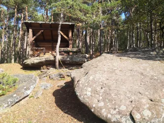 Eine Schutzhütte steht zwischen großen Felsen im Wald. Die Umgebung ist grün und idyllisch. Hier die Schutzhütte am neuen Teufelsfelsen, hoch über Lambrecht (Pfalz) zu sehen.