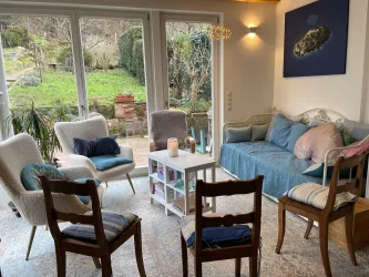 Ein helles Wohnzimmer mit bequemen Sofas und Stühlen. Große Fenster bieten einen Blick auf den Garten. Dieser Raum wird für Trauergruppen genutzt.