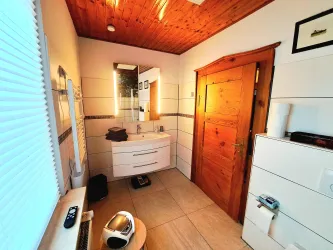 Ein modernes Badezimmer mit einer hellen Holzdecke und einer großen Spiegelwand. Die Tür ist aus Holz und es gibt verschiedene Badezimmermöbel und Accessoires.