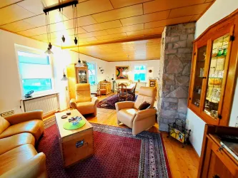 Ein gemütliches Wohnzimmer mit Ledermöbeln und einem Holztisch. Es gibt Teppiche, einen Kamin und große Fenster, die viel Licht hereinlassen.