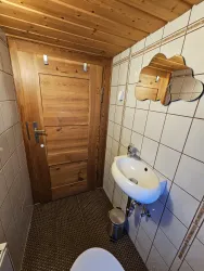 Ein kleines Badezimmer mit Holzdekor und gefliesten Wänden. Es enthält ein Waschbecken, eine Toilette und eine Holzverkleidung an der Decke.