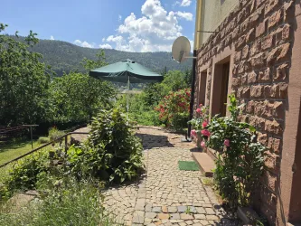 Ein schöner Gartenweg mit bunten Blumen und grünen Pflanzen. Im Hintergrund ist ein großes Sonnensegel und die umliegenden Berge sichtbar.