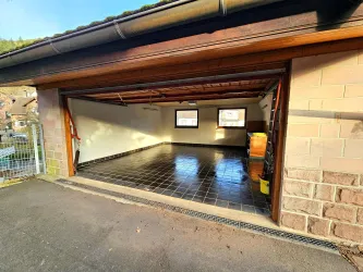 Eine leere Garage mit fliesenboden und Holzdecke. Es gibt große Fenster, die Tageslicht hereinlassen.