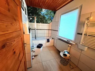 Ein modernes Badezimmer mit einem Fenster, das einen Blick ins Freie bietet. Es gibt eine Badewanne, eine Toilette und einen Handtuchhalter an der Wand.