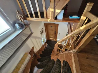 Eine helle Treppe aus Holz mit einer spiralförmigen Form. Im Hintergrund ist eine Eingangstür und ein Fenster zu sehen.