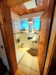 Ein modernes Badezimmer mit Holzdetails und großem Fenster. Es gibt eine Dusche, ein Waschbecken und helle Fliesen.