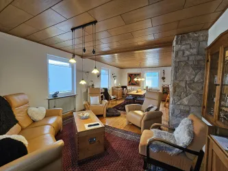 Ein gemütliches Wohnzimmer mit hellen Möbeln und einer Holzdecke. Der Raum ist freundlich und einladend gestaltet.