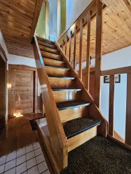 Eine Holztreppe führt nach oben in einen gemütlichen Flur. Die Wände sind hell und der Boden hat einen warmen Farbton.