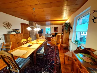 Ein gemütliches Wohnzimmer mit einem großen Esstisch aus Holz und vielen Stühlen. Das Zimmer hat viel Tageslicht und eine warme Atmosphäre.