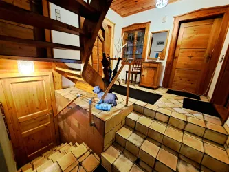 Ein heller Eingangsbereich mit Holztreppe und gefliesten Böden. Links sind mehrere Türen und eine Garderobe zu sehen.