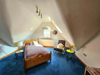 Ein gemütliches Schlafzimmer mit einem Holzbett und blauem Teppich. Der Raum hat eine freundliche Atmosphäre und viel Tageslicht.