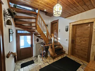 Ein einladender Eingangsbereich mit einer Holztreppe und einem schönen Kronleuchter. Der Boden ist gefliest und die Wände sind in warmen Holztönen gehalten.