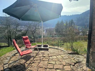 Ein schöner Außenbereich mit zwei roten Liegestühlen und einem Sonnenschirm. Im Hintergrund sind Bäume und ein weites Tal zu sehen.