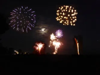 Ein farbenfrohes Feuerwerk erleuchtet den Nachthimmel. Im Hintergrund ist der Vollmond sichtbar.