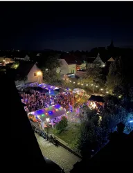 Eine lebhafte Nachtveranstaltung mit bunten Lichtern und vielen Menschen. Zelte und festliche Dekorationen schaffen eine fröhliche Atmosphäre.