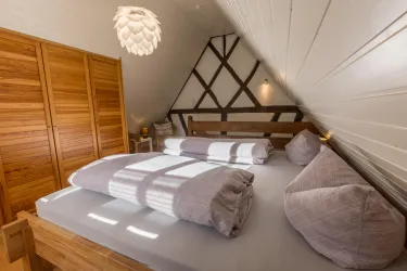 Ein gemütliches Schlafzimmer mit einem Doppelbett und Holzdetails. Der Raum hat eine warme Atmosphäre und viel natürliches Licht.