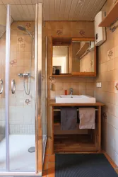 Ein modernes Badezimmer mit einer Dusche und einem Waschbecken aus Holz. Die Wände sind mit beigen Fliesen und Blumenmuster dekoriert.