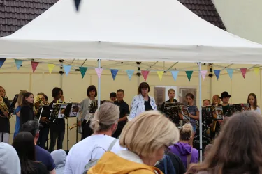 Eine Gruppe junger Musiker spielt unter einem Zelt. Im Hintergrund sind Zuschauer zu sehen, die der Aufführung zuhören.