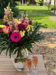 Ein schöner Blumenstrauß mit bunten Blumen steht in einer Vase. Im Vordergrund sind zwei Gläser mit Sekt zu sehen.