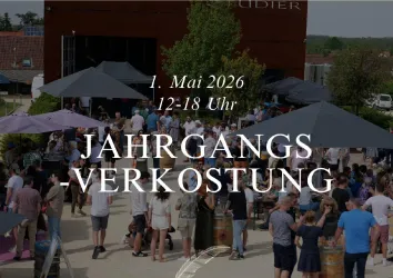 Eine lebendige Veranstaltung im Freien mit vielen Menschen, die sich unter Sonnenschirmen versammeln. Im Hintergrund ist ein Gebäude zu sehen, das zu einer Weinfirma gehört.