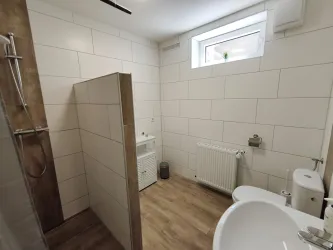Ein modernes Badezimmer mit einer Dusche und einem Waschbecken. Es hat helle Fliesen und ein Fenster für Tageslicht.