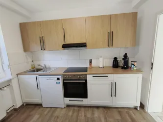 Eine moderne Küche mit Holzschränken und weißen Fronten. Es gibt einen Herd, eine Spüle und verschiedene Küchengeräte.